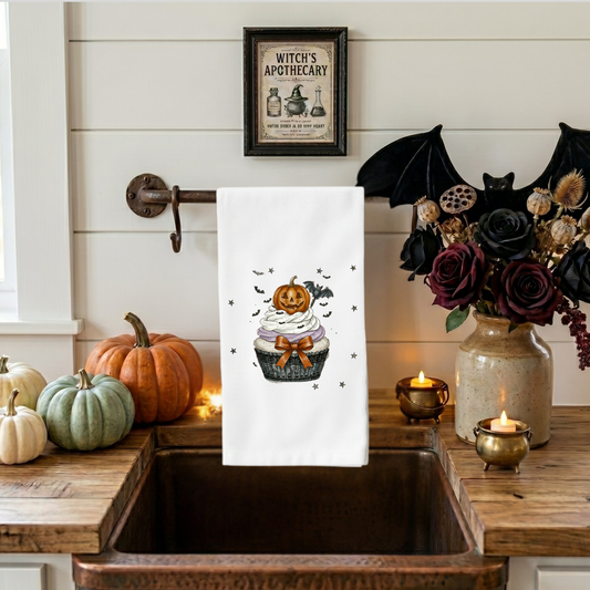 Pumpkin cupcake Halloween kitchen towel featuring a jack-o'-lantern topper, bats, stars, and orange bow on a white flour sack towel