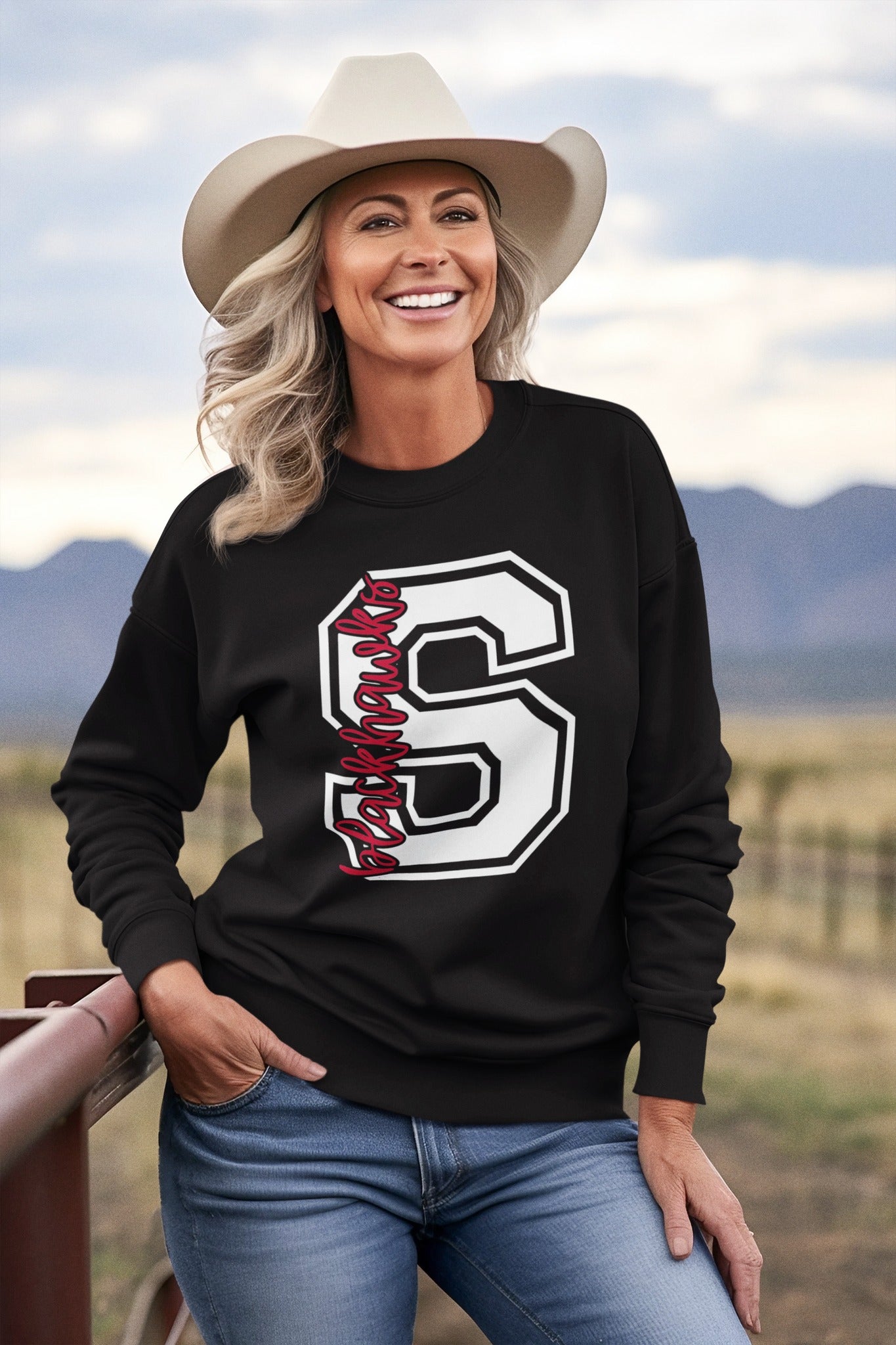 Woman wearing a black Sheridan Blackhawks varsity letter S crewneck with black detailing, standing outdoors.