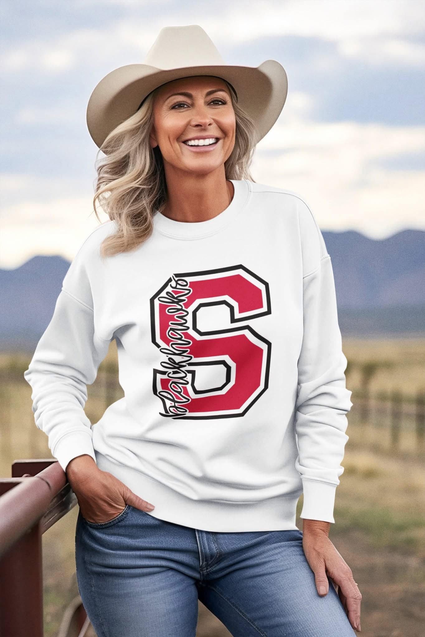 Woman wearing a white Sheridan Blackhawks varsity letter S crewneck with black detailing, standing outdoors.