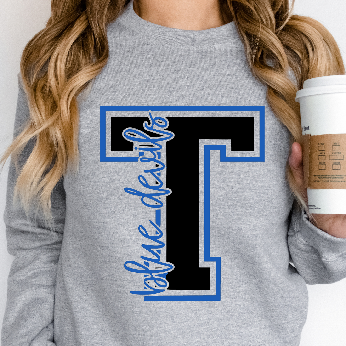 Woman wearing Tipton Varsity T Heather Crewneck Sweatshirt featuring classic Blue Devils spirit wear design, holding a coffee cup.