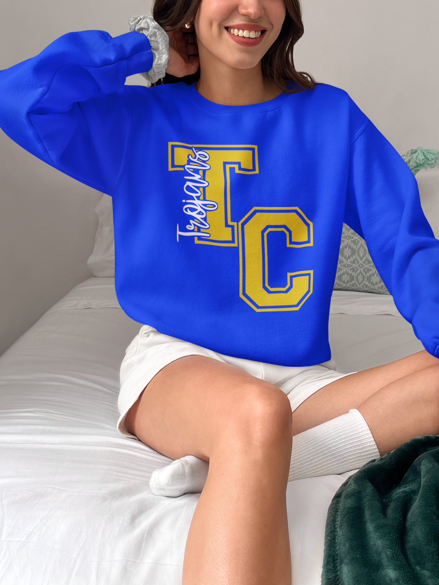 Woman wearing royal blue Tri-Central Trojans varsity TC crewneck sweatshirt while sitting on a bed
