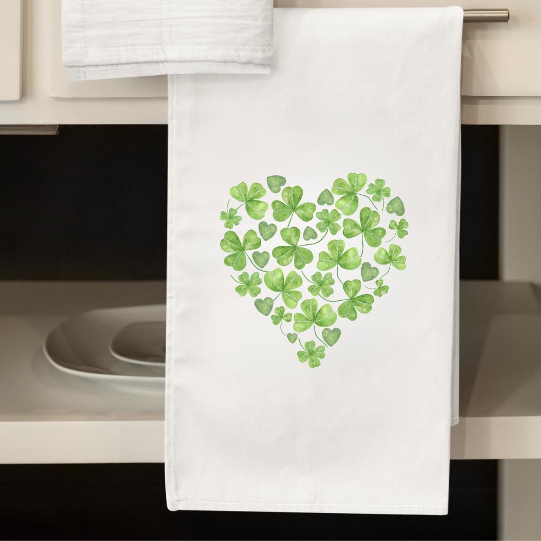 White flour sack towel featuring a heart shape made of clovers and hearts.