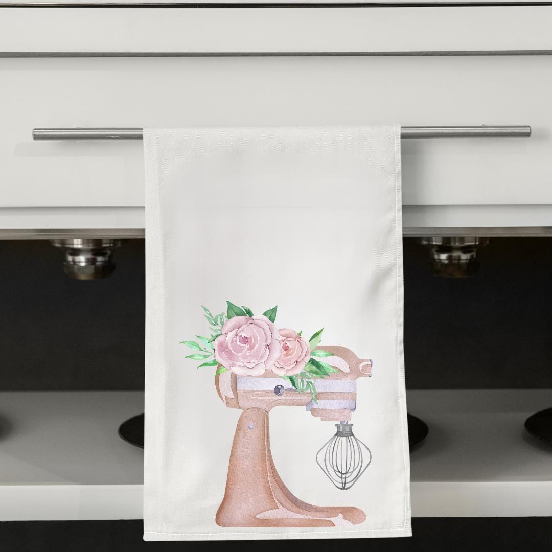 Kitchen towel with a mixer and floral design hanging on a cabinet.