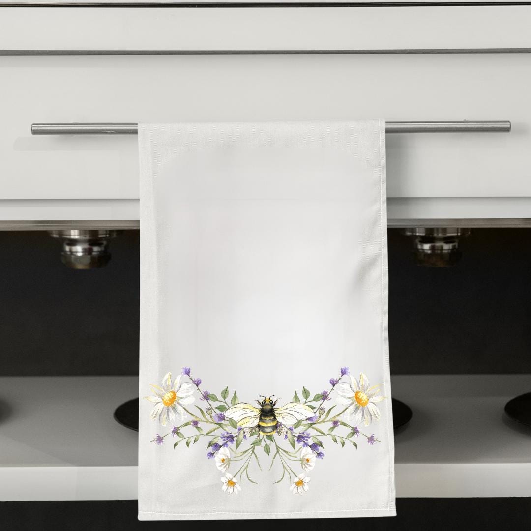 White towel with a bee and floral design hanging on a kitchen towel rack.