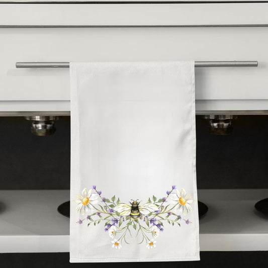 White towel with a bee and floral design hanging on a kitchen towel rack.
