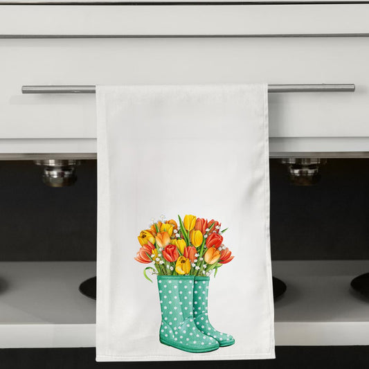 May include: White kitchen towel with a watercolor illustration of a bouquet of tulips in a pair of teal polka-dot rain boots. The tulips are yellow, orange, and red. The towel is hanging on a silver bar.