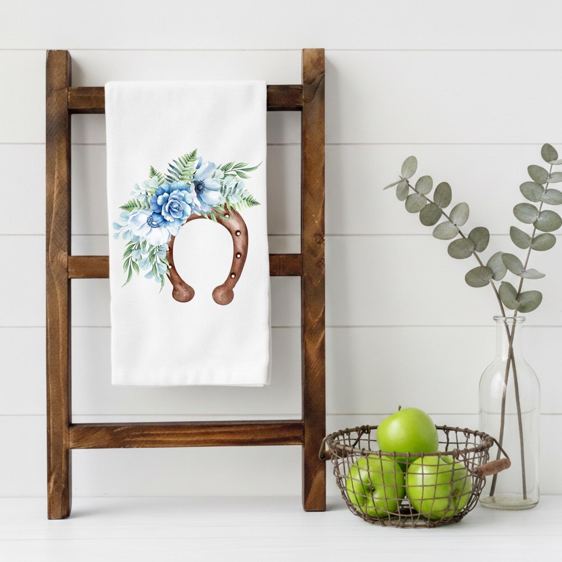 Decorative towel with floral horseshoe design on a wooden ladder against a white wall.