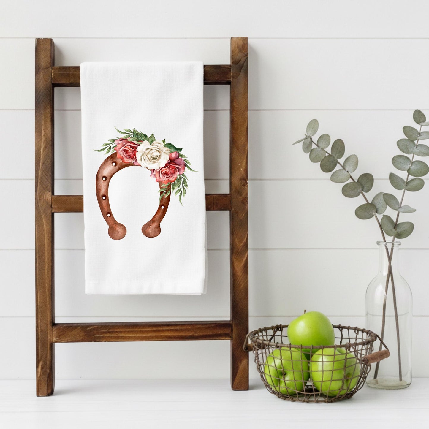 Floral design towel on a wooden ladder with a basket of apples and a vase of eucalyptus.