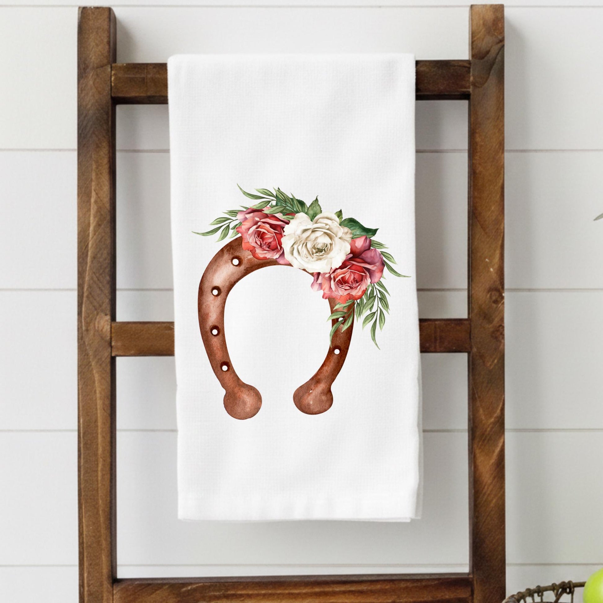 Floral horseshoe design on a white towel hanging on a wooden ladder.