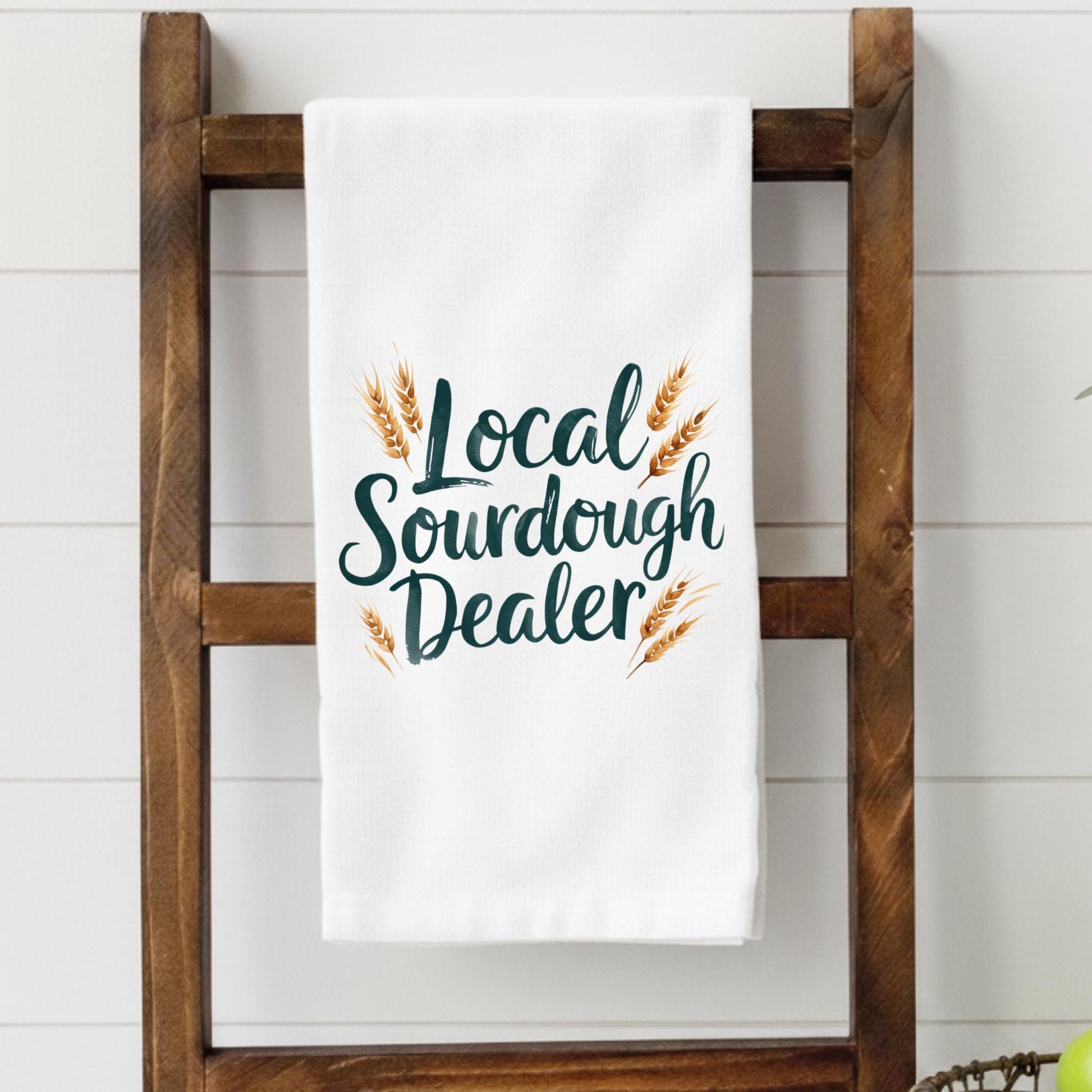 White towel with 'Local Sourdough Dealer' text and wheat graphics on a wooden towel rack.