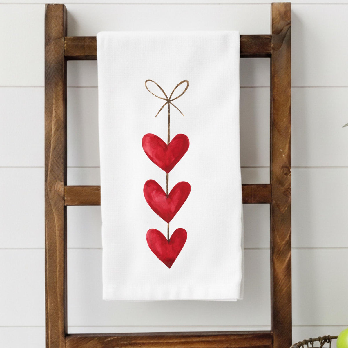 White towel with red heart design on a wooden ladder against a white wall.