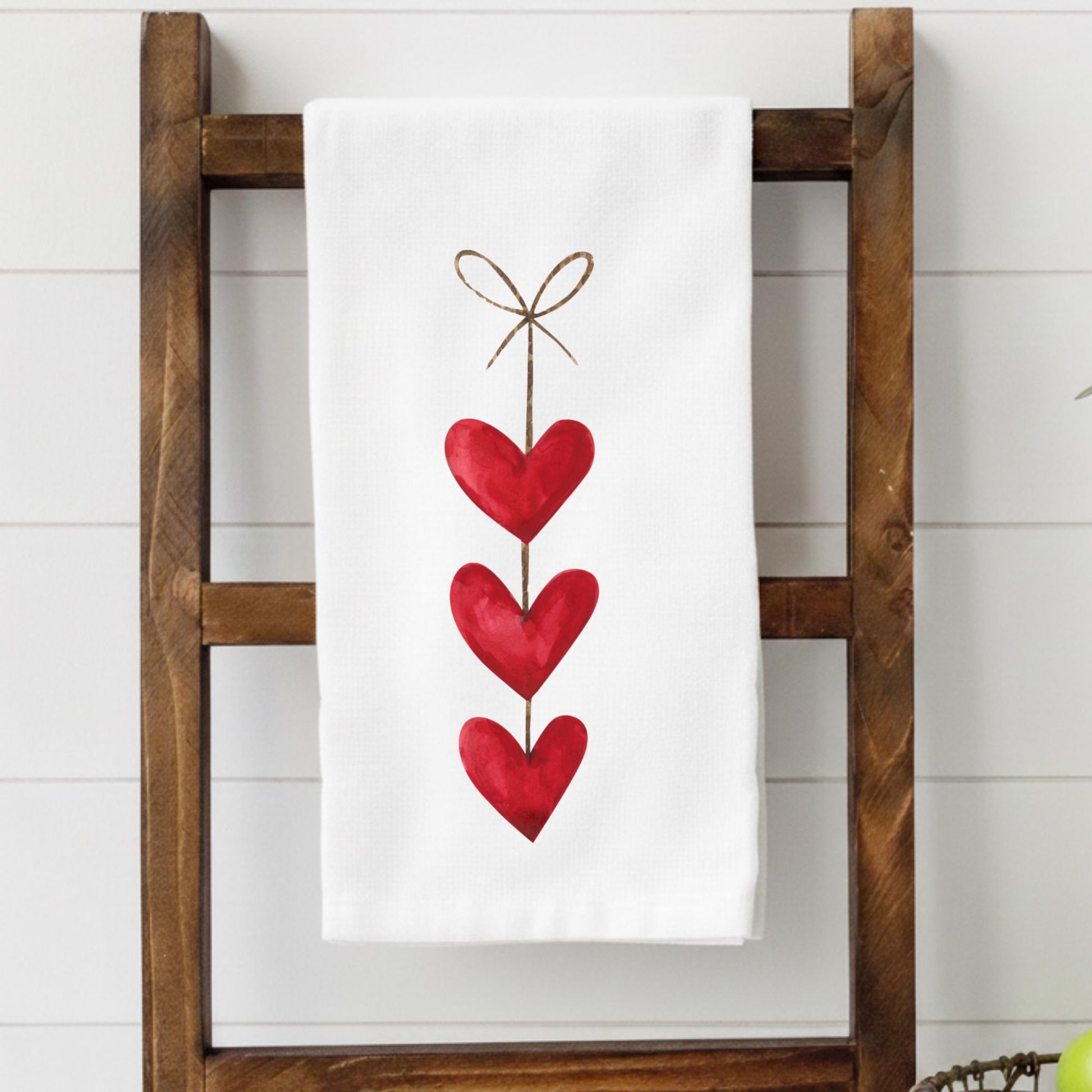 White towel with red heart design on a wooden ladder against a white wall.