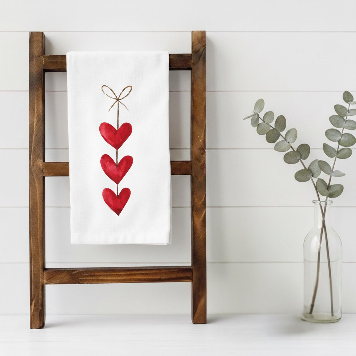 White towel with red heart design on a wooden ladder against a white wall.
