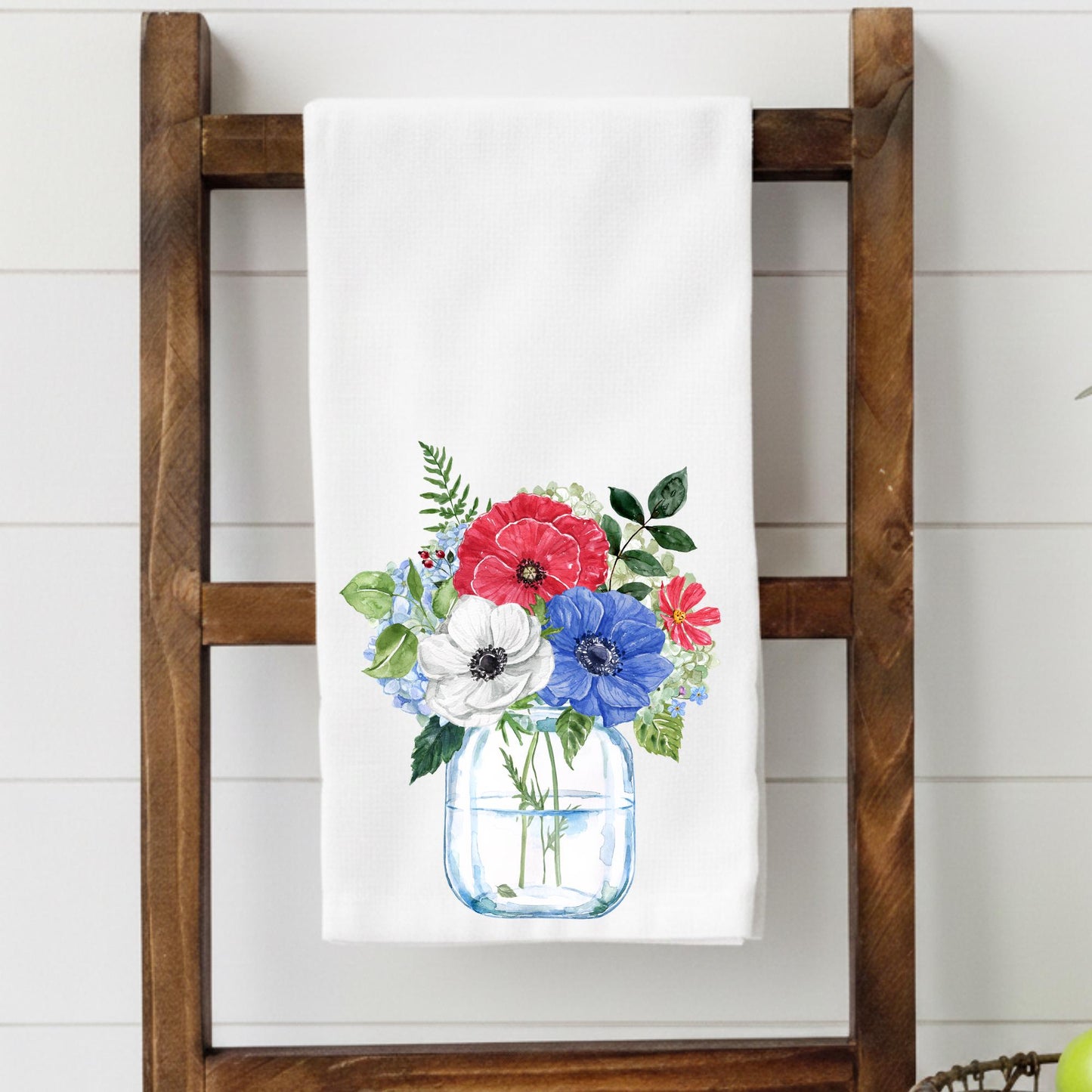 Floral towel with a jar of flowers design on a wooden ladder against a white wall.