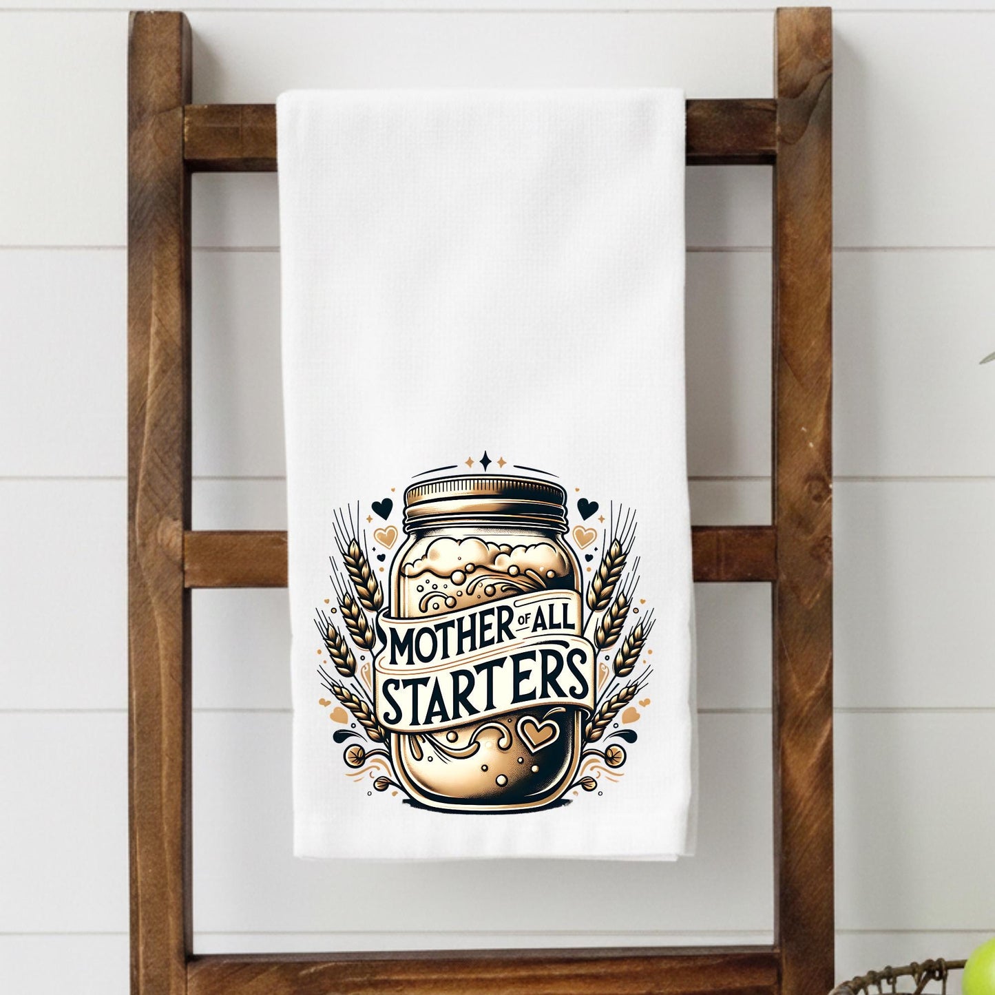 Towel with 'Mother of All Starters' design on a wooden towel rack.