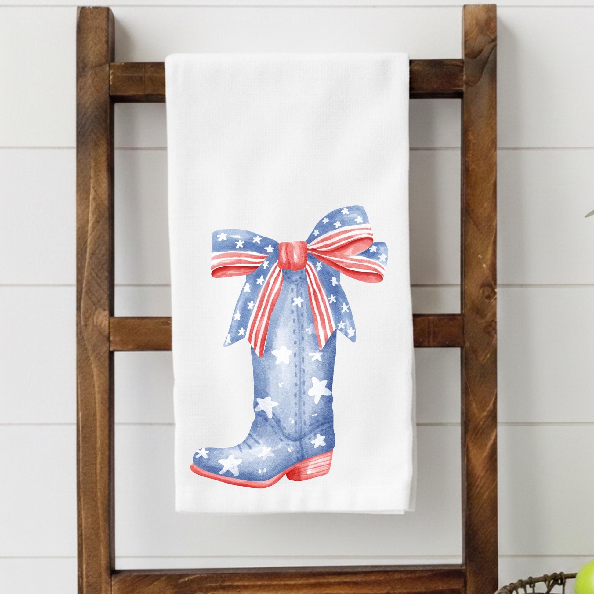 Towel with a design of a blue boot with stars and a red bow hanging on a wooden ladder.
