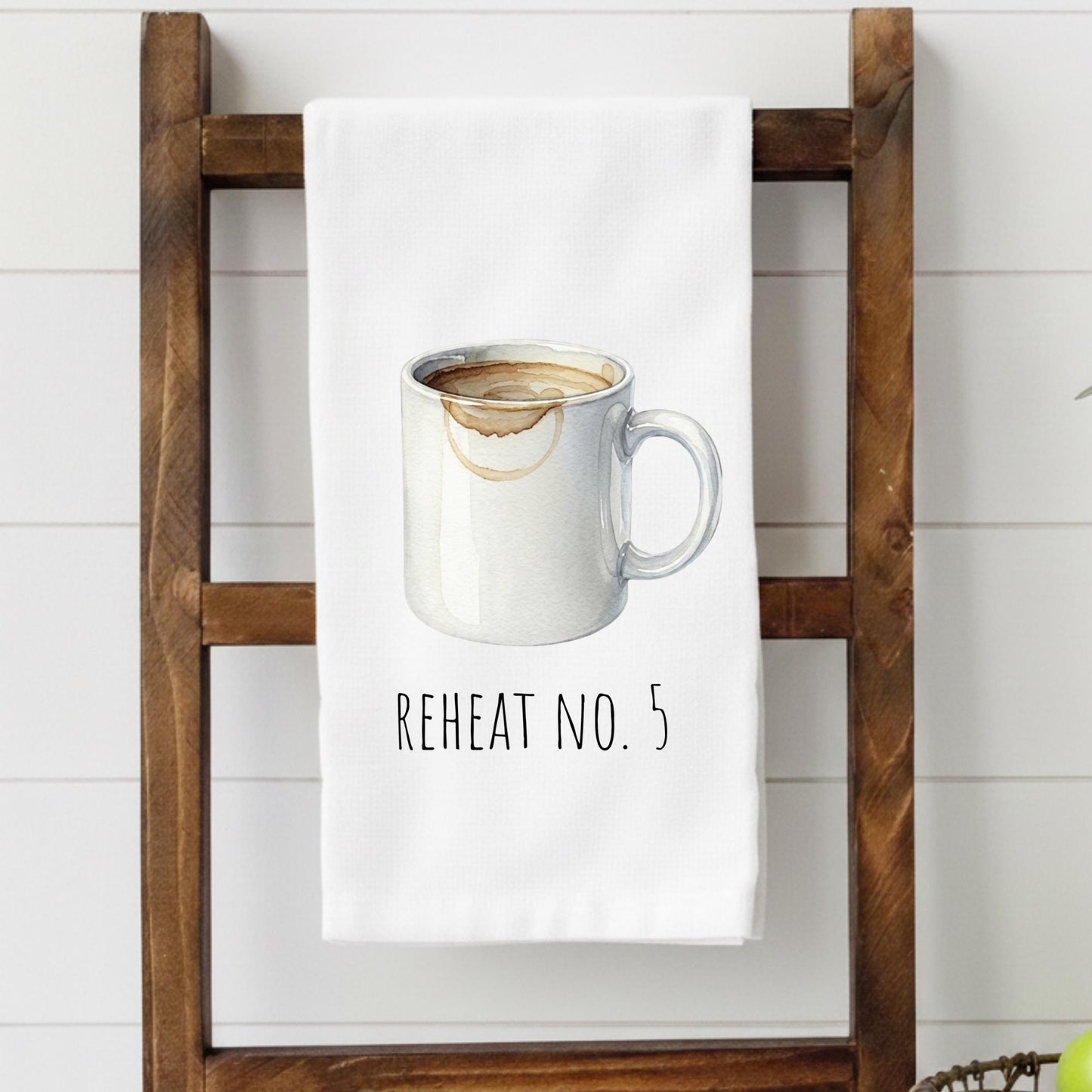 White towel with a graphic of a coffee mug and text 'REHEAT NO. 5' hanging on a wooden rack.