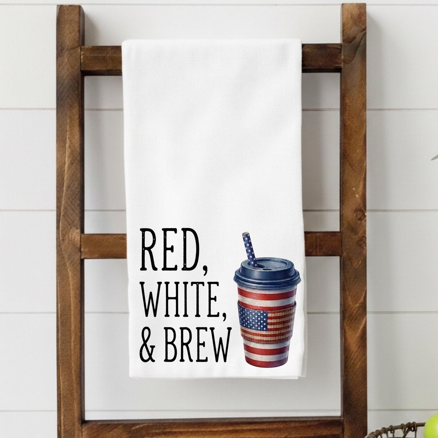 Towel with 'Red, White, & Brew' text and coffee cup graphic on a wooden ladder.