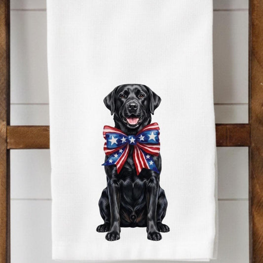 Black dog wearing a red, white, and blue bow tie on a white towel.