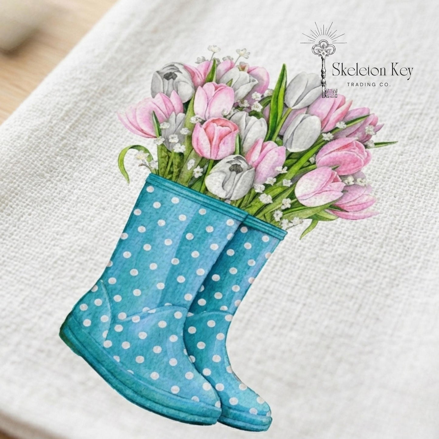 Blue polka dot rain boot with pink and white tulips on a white background, featuring 'Skeleton Key Trading Co' logo.
