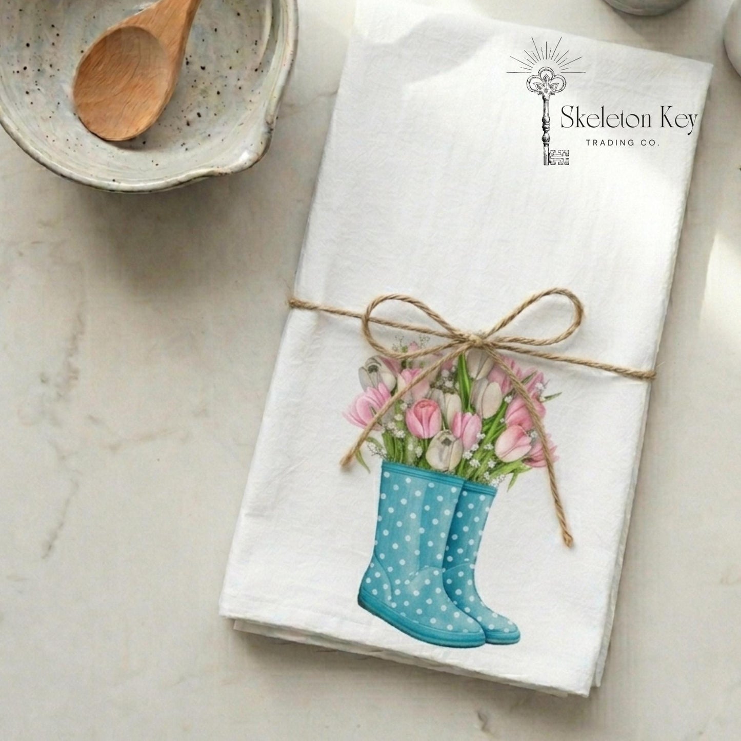 Folded napkin with a design of blue rain boots and pink tulips, tied with twine, on a marble surface.
