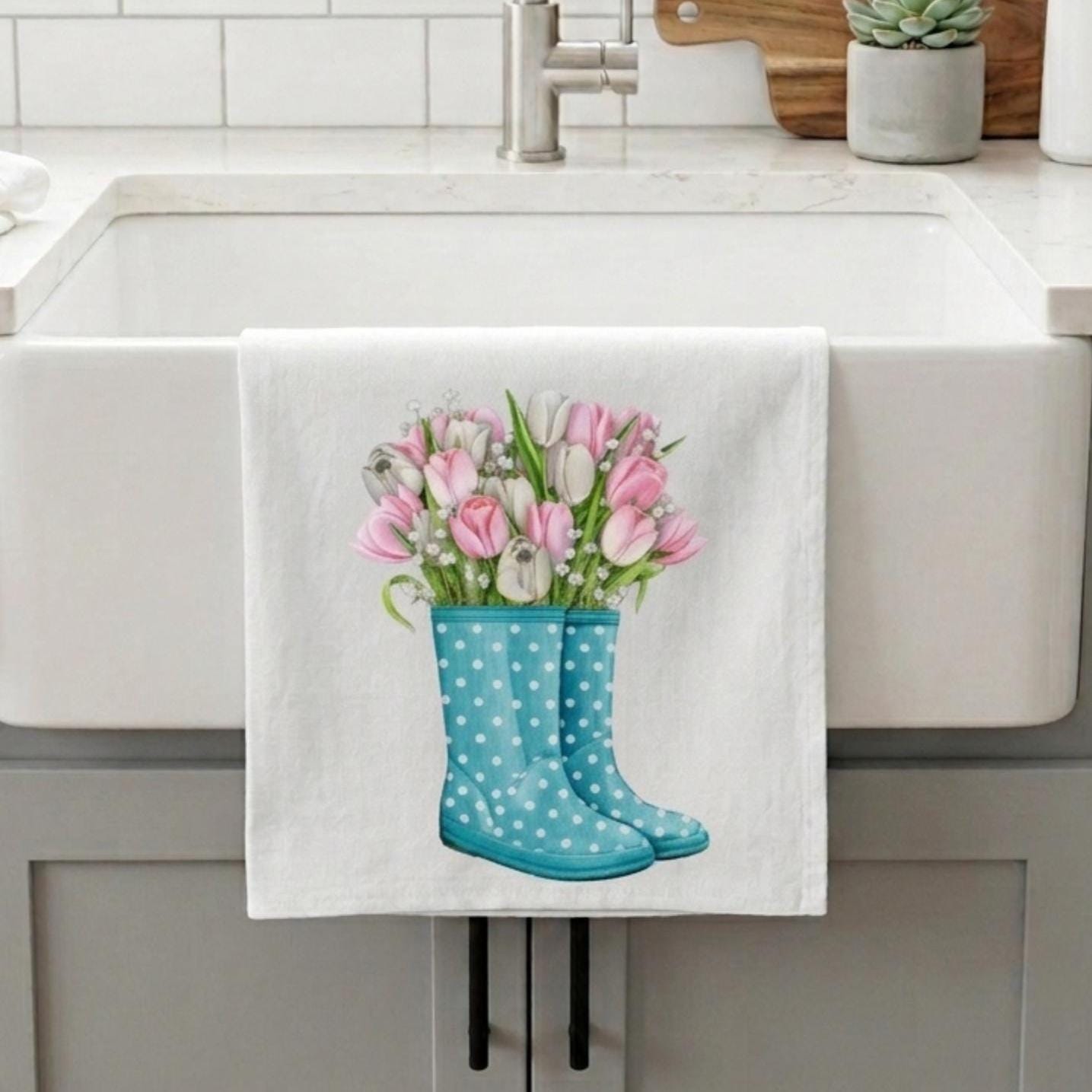 Kitchen towel with blue rain boots and pink tulips hanging over a sink.