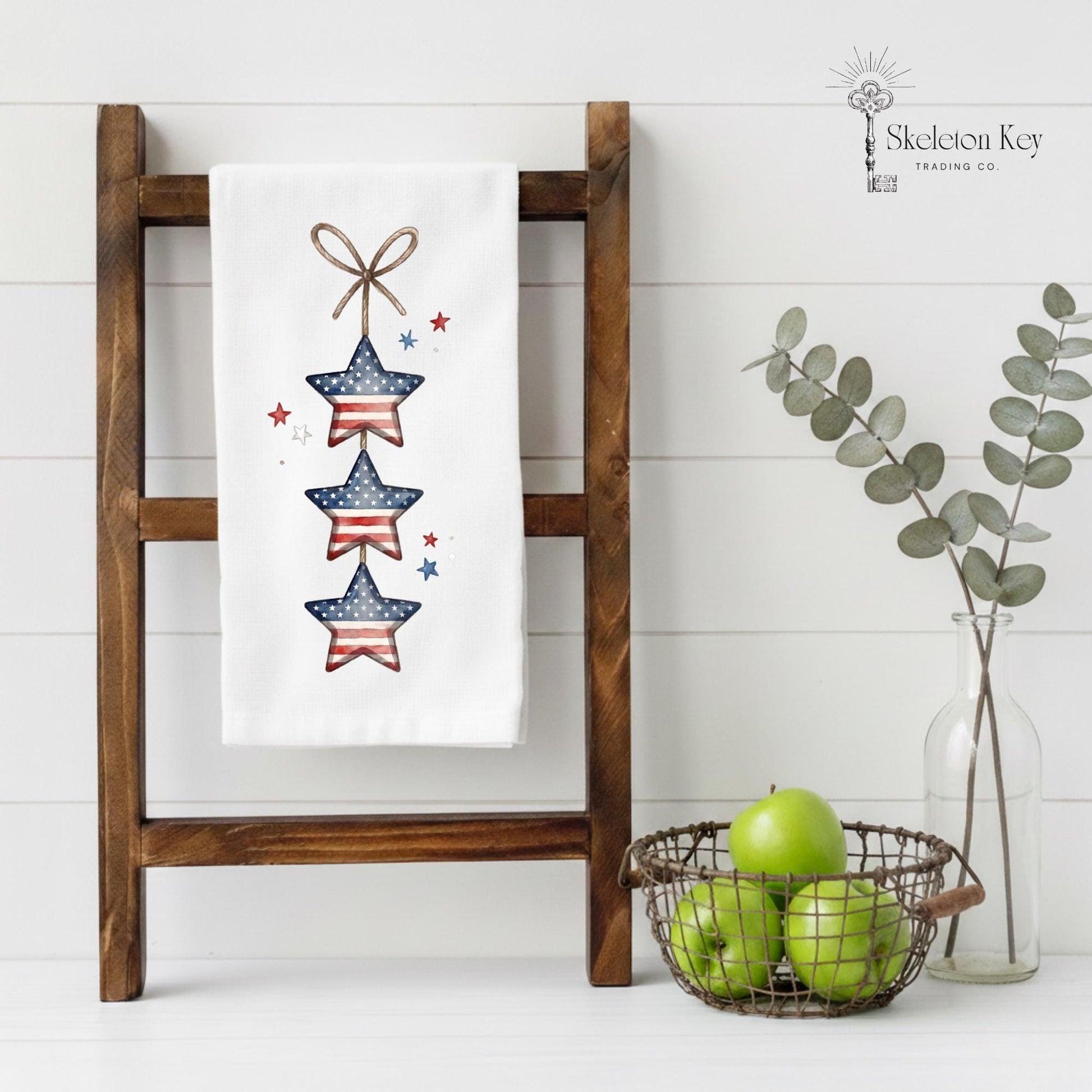 Decorative towel with star design on a wooden ladder against a white wall, with a basket of apples and a vase of eucalyptus.