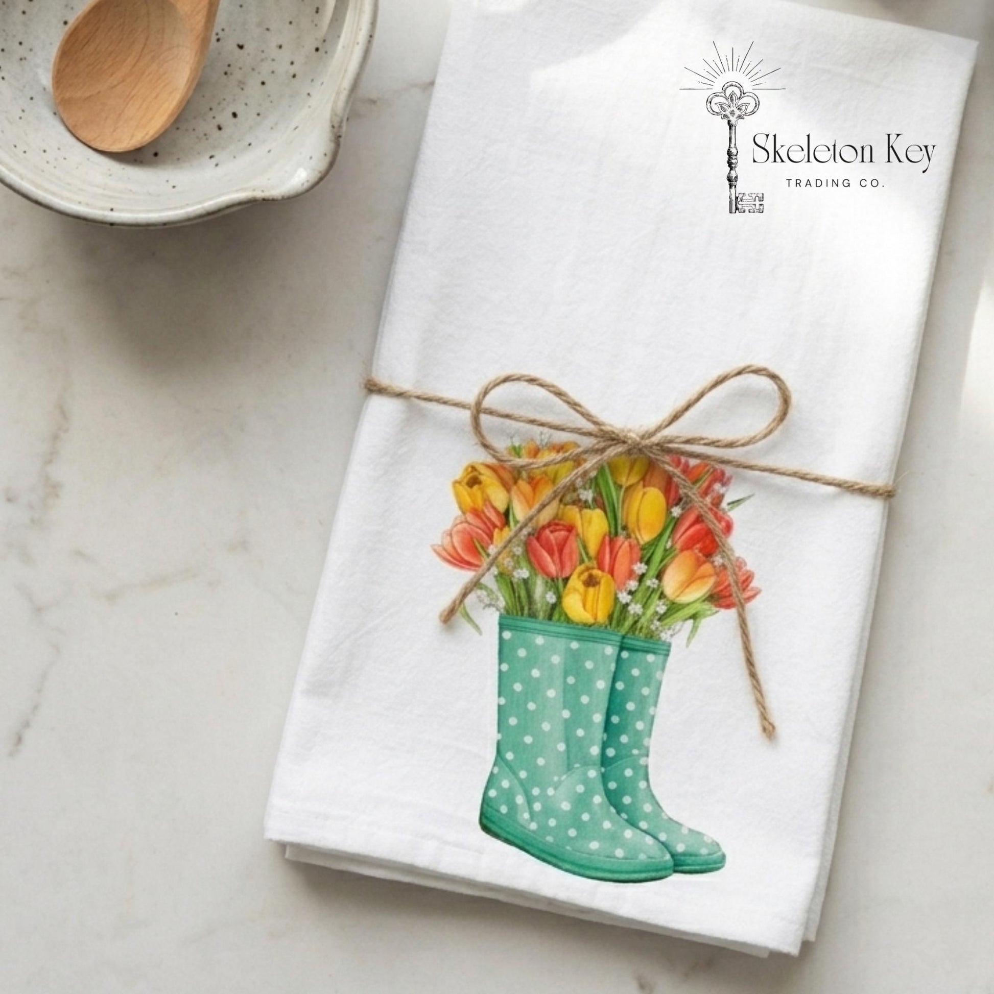 Folded towel with a design of green wellies and tulips, tied with twine, on a marble surface.