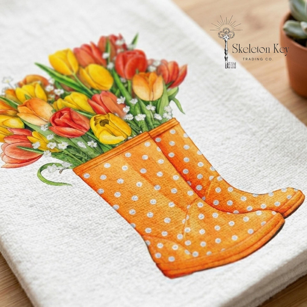 Close-up view of an illustration of orange rainboots with white polka dots and colorful flowers in the boots on a flour sack tea towel.
