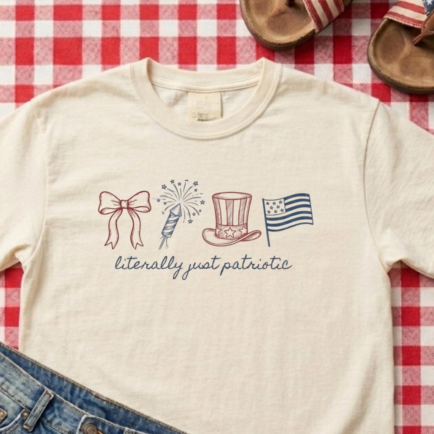 May include: Cream-colored t-shirt with a patriotic design. The design includes a bow, fireworks, a top hat, and a flag, all in red and blue. The text "literally just patriotic" is written below the illustrations.