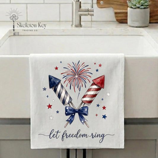 Patriotic tea towel hanging on farmhouse sink featuring fireworks rockets and Let Freedom Ring artwork