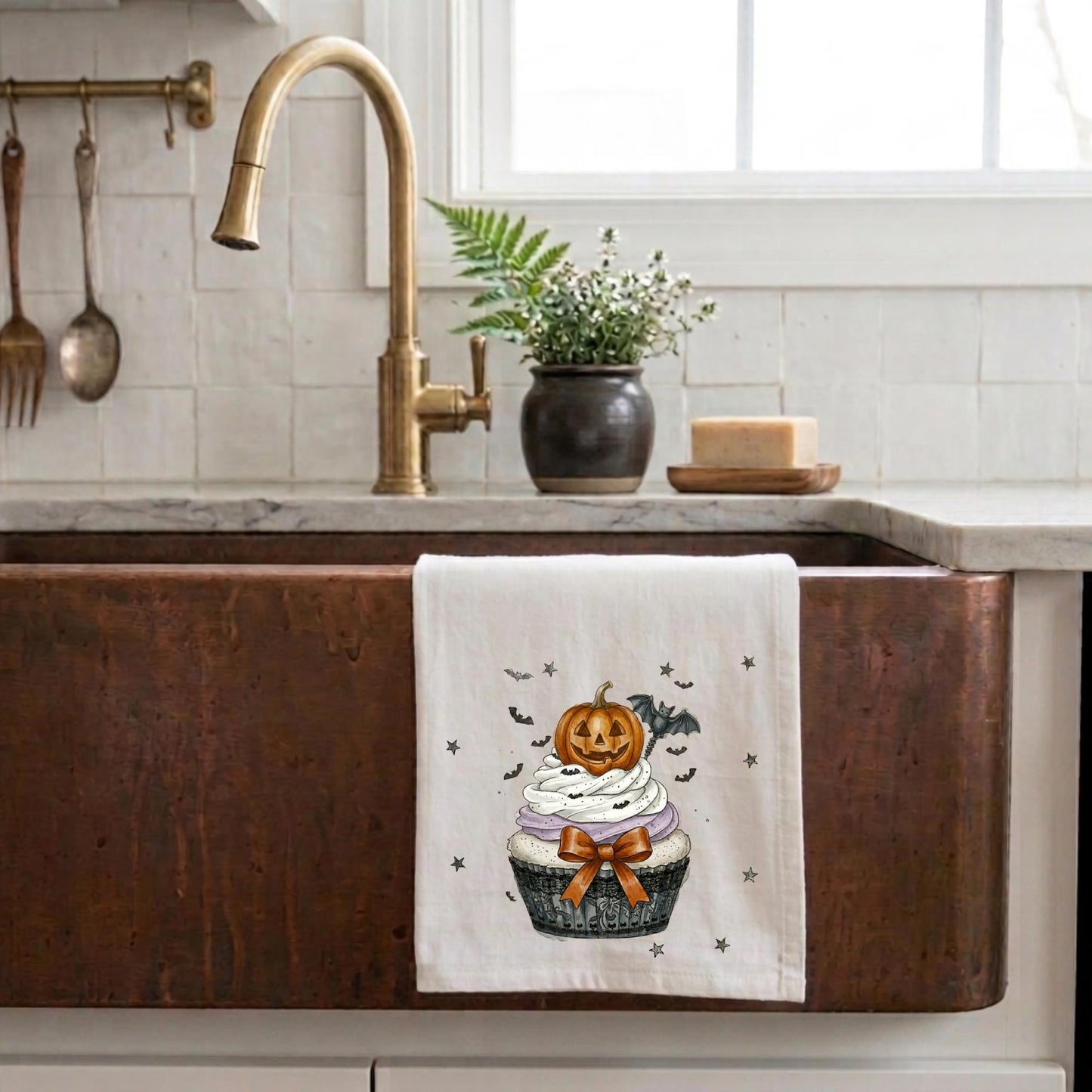 Cute Halloween tea towel featuring a pumpkin cupcake design displayed on a rustic copper farmhouse sink
