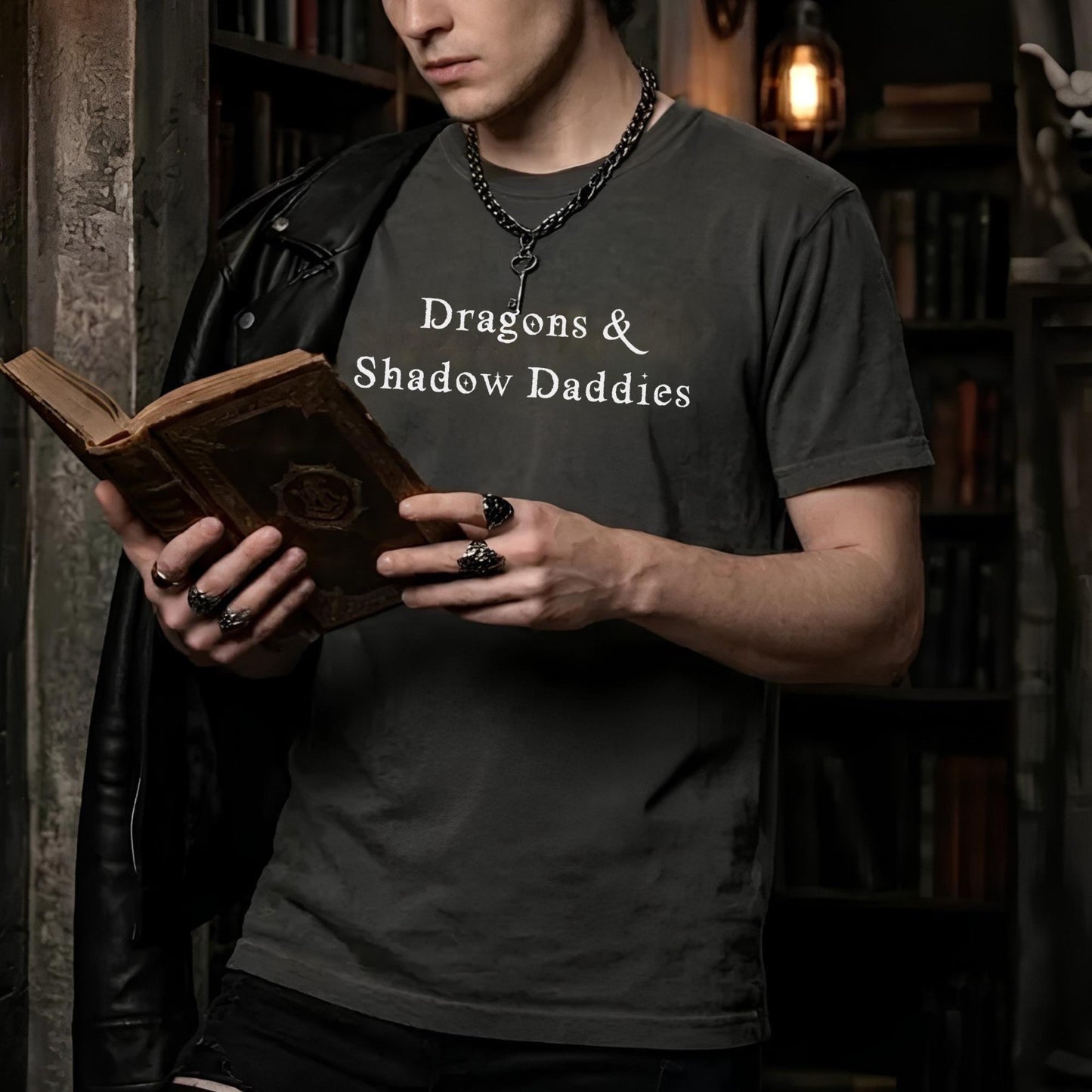 Man wearing Dragons & Shadow Daddies shirt while reading a fantasy novel in a dark academia library setting