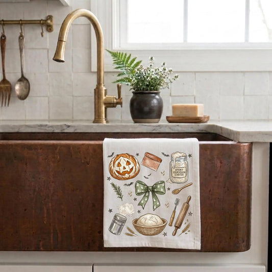 Kitchen sink with a decorative towel featuring baking illustrations, gold faucet, and potted plant.