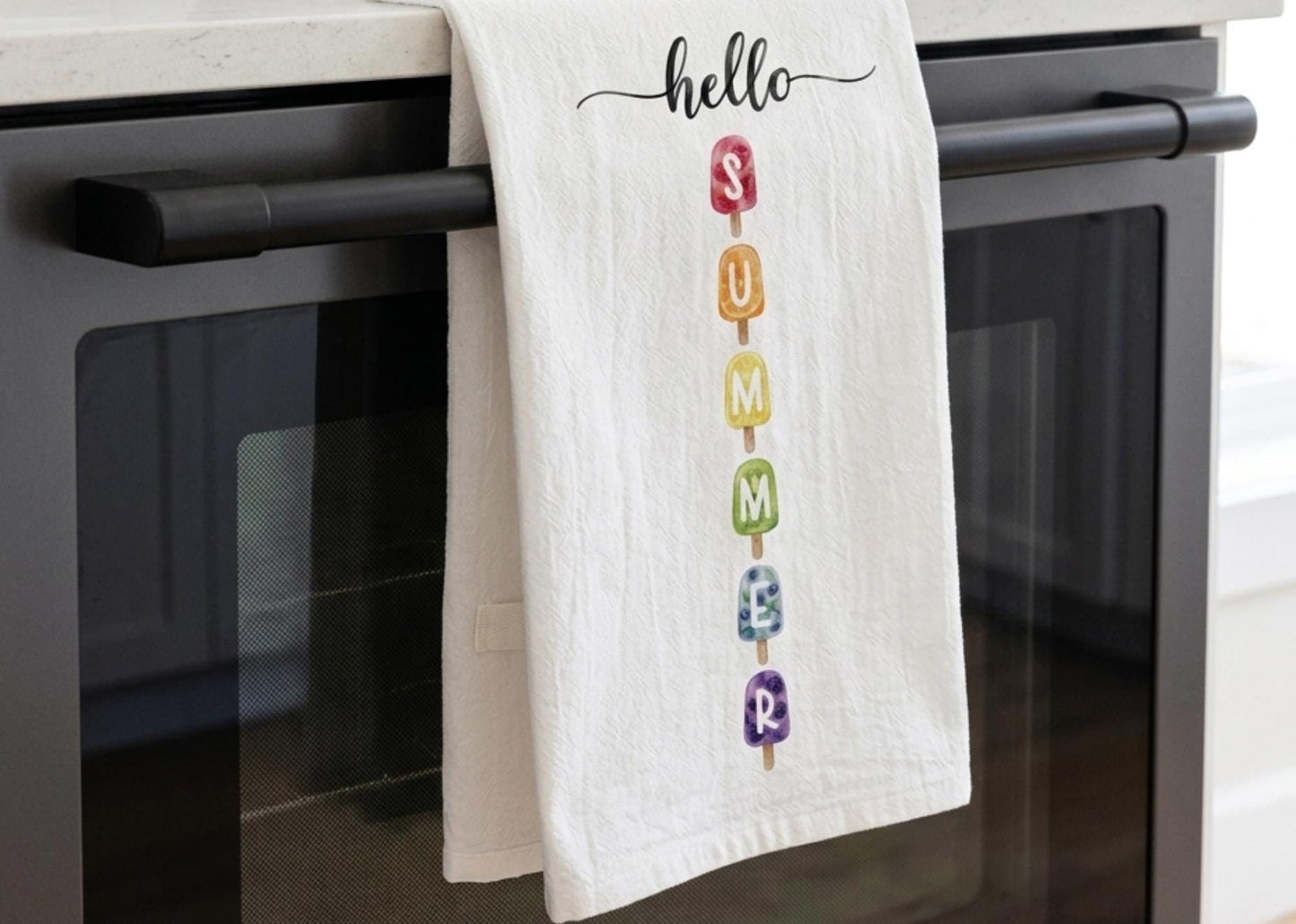 White towel with colorful 'hello summer' design hanging on a kitchen appliance.