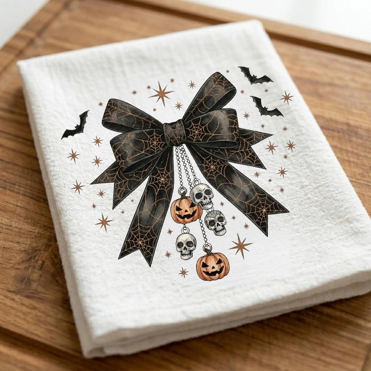 White napkin with Halloween-themed design featuring a black bow, pumpkins, and skulls on a wooden surface.