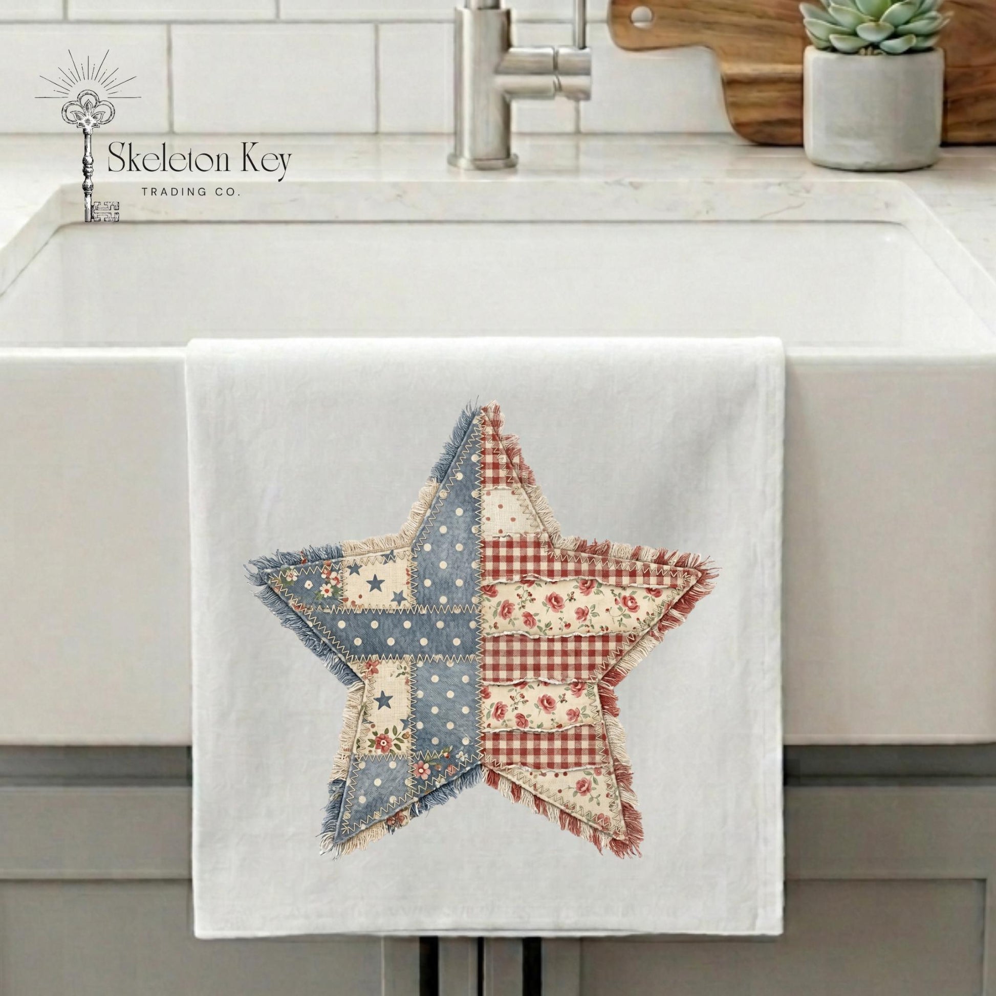 A white kitchen towel draped over a white farmhouse sink, featuring a large patchwork star design in blue, red, and cream floral print. The image has the 'Skeleton Key Trading Co' logo in the upper left corner.