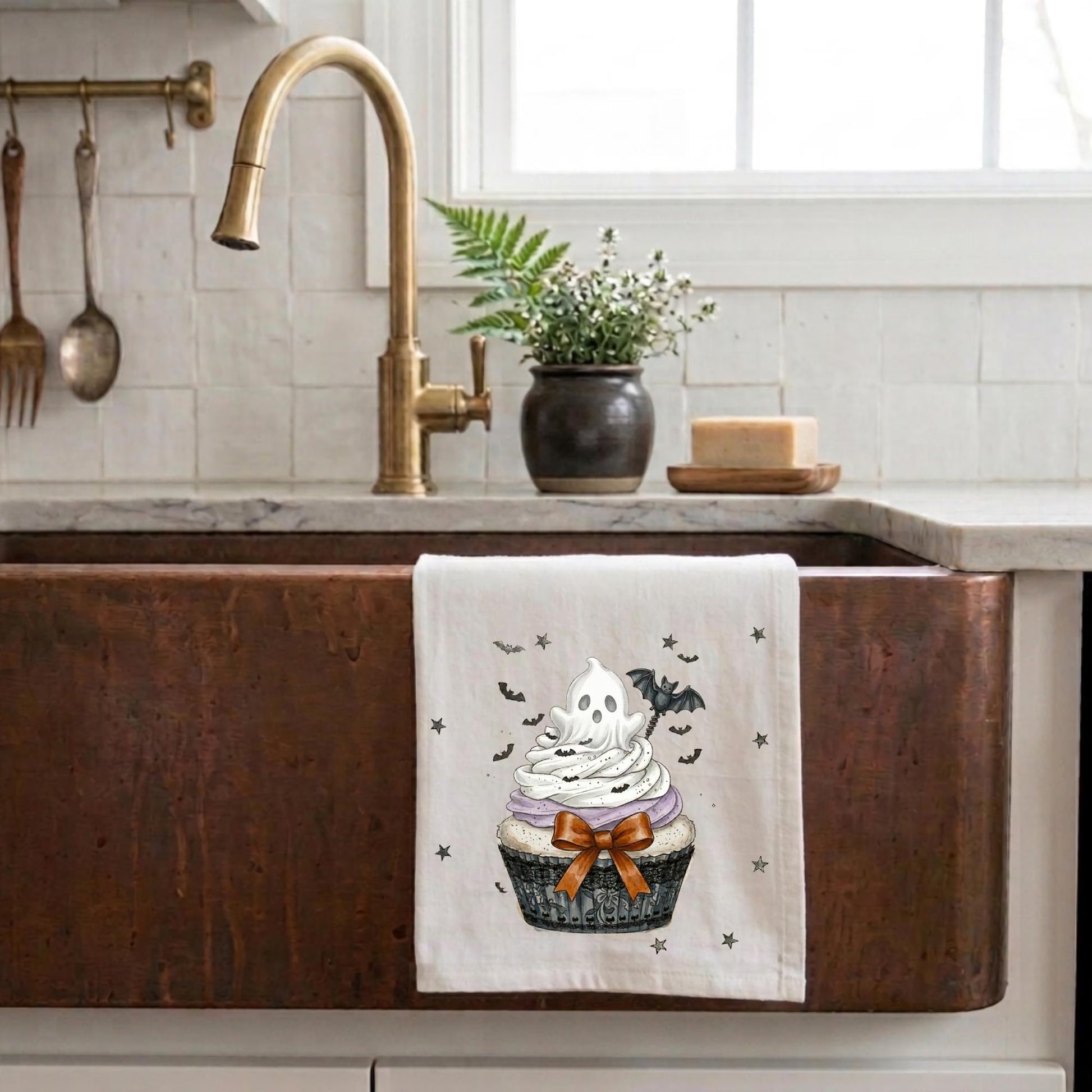 Cupcake-themed towel hanging on a copper kitchen sink with decorative elements.
