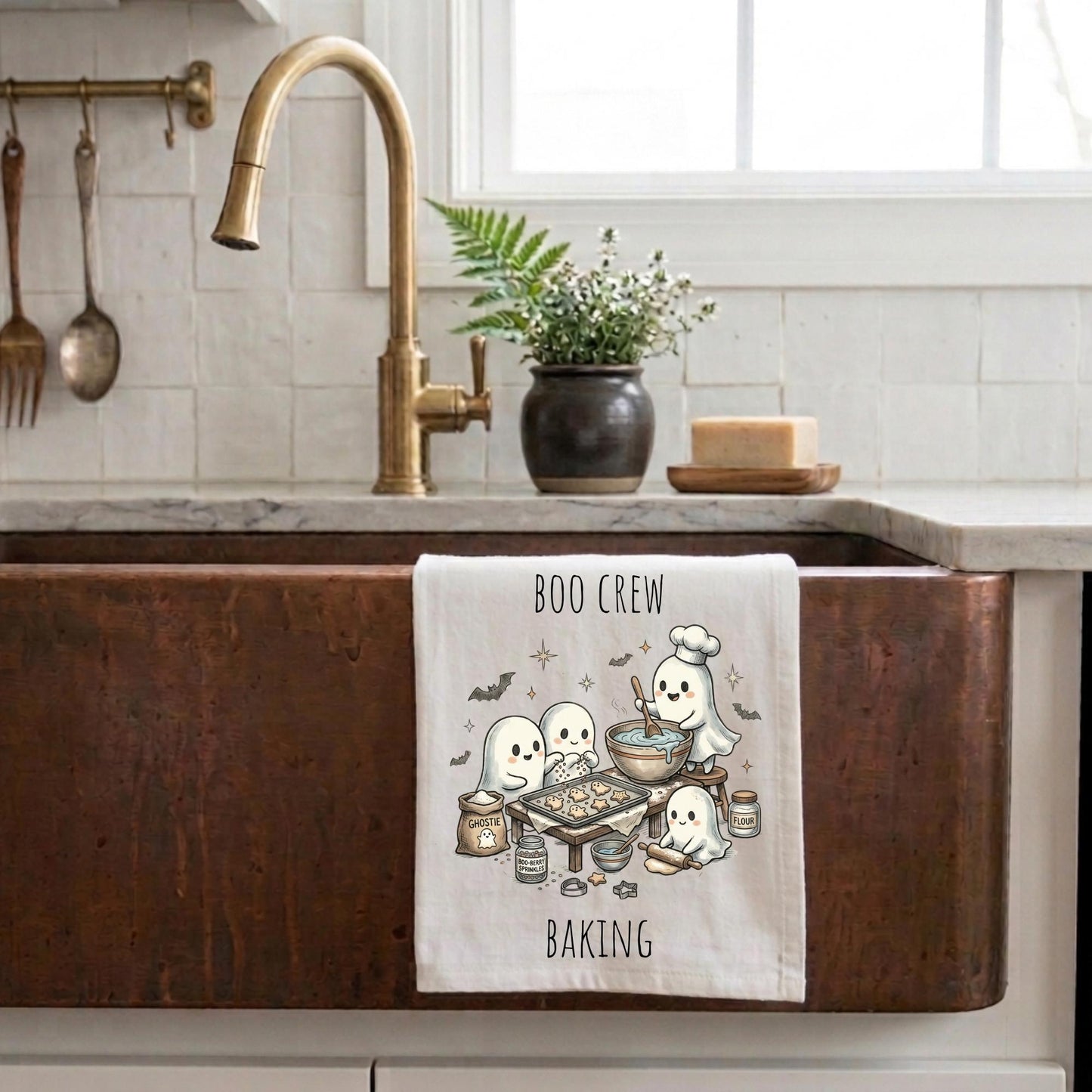 Kitchen sink with a decorative towel featuring pumpkins, gold faucet, and white tiled wall.